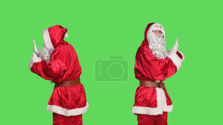 Photo for Saint nick pushing object left or right, pretending to refuse something against isolated greenscreen background. Young adult in santa festive costume doing rejection symbol aside. - Royalty Free Image