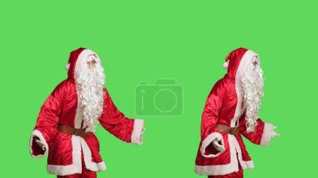 Photo for Model in santa claus suit with beard feeling positive about festive season, celebrating christmas eve holiday over greenscreen background. Joyful man advertising december celebration. - Royalty Free Image