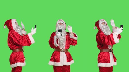 Téléchargez les photos : Homme Santa Claus sur vidéocall réunion, avoir du plaisir à parler à quelqu'un en utilisant le chat de téléconférence en ligne. Jeune homme habillé comme le père Noël assister à la conférence sur écran vert. - en image libre de droit