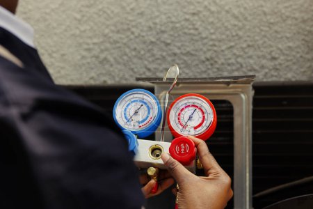 Photo for Pressure indicator tool able to find malfunctioning expansion valve and other issues, close up. Technician using manifold benchmarking gadget to read refrigerant levels of outdoor air conditioner - Royalty Free Image