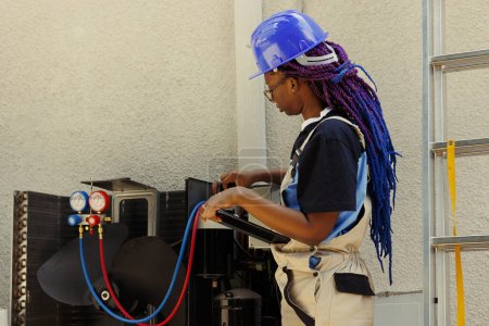 Photo for Electrician looking online for new evaporator coil after finding out of order condenser component during annual maintenance. African american expert checking air conditioner internal part stock - Royalty Free Image