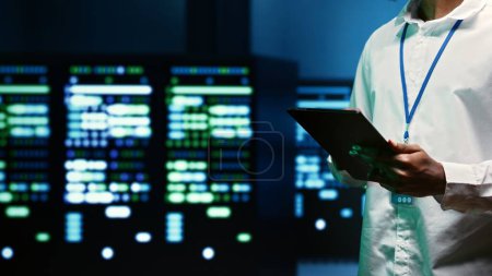 Photo for IT specialist walking through server rows performing data backups, close up. Serviceman using tablet to make sure electric generators are able to ensure operational continuity - Royalty Free Image
