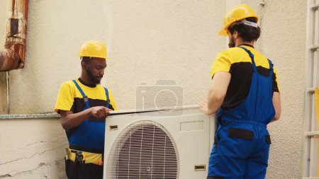 Photo for Teamworking licensed servicemen starting work on faulty hvac system, taking apart condenser coil panel. Qualified electricians disassembling air conditioner to check for improper wiring - Royalty Free Image