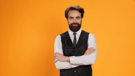 Photo for Before serving meal, elegant waiter poses with reliability in front of a yellow background in studio. Bearded server in suit operating in formal environment in the culinary sector. - Royalty Free Image