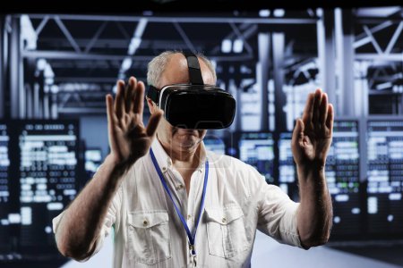 Photo for Elderly adept technician immersed in virtual reality at data center, doing infrastructure maintenance. Specialist using VR headset to optimize server clusters system performance - Royalty Free Image