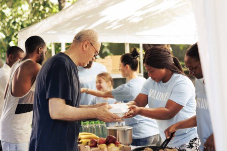 Téléchargez les photos : Les jeunes bénévoles du centre local donnent de la nourriture gratuite à divers groupes de sans-abri qui bénéficient de la campagne alimentaire caritative. Les œuvres de charité partagent des repas gratuits pour les affamés et les pauvres. - en image libre de droit