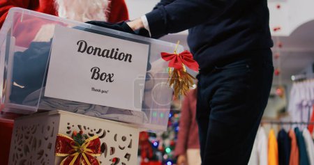 Photo for Close up shot of charity box in xmas ornate clothing store. Caring community touched by Christmas spirit donating clothes for philantropy efforts during festive holiday season - Royalty Free Image