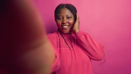 Photo for African american female vlogger talking on online video call with webcam, grasping smartphone. Enthusiastic black woman doing vlog content with digital mobile phone against vibrant pink background. - Royalty Free Image