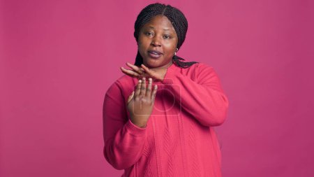 Photo for Expressive young black woman showing time-out sign using her hands in front of pink background. African american beauty displaying pause-break signal with body language towards camera. - Royalty Free Image