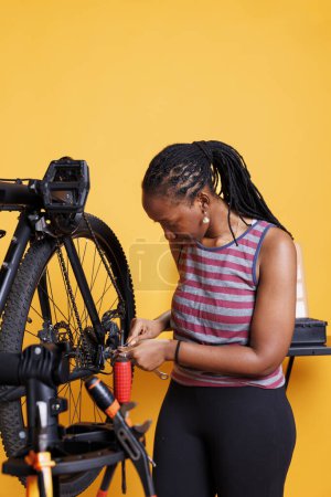 Photo for African american female cyclist adjusts and repairs bicycle components with specialized toolkit, ensuring optimal performance. Sporty black woman using wrench to for bike wheel adjustment. - Royalty Free Image