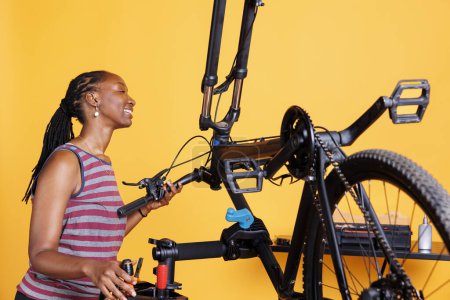 Photo for Athletic black woman engrossed in fixing broken bike components with specialist tools. African american lady expertly adjusting, examining, and repairing bicycle parts for optimal performance. - Royalty Free Image