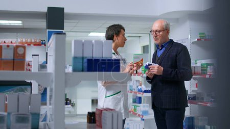 Älterer Mann, der sich unwohl fühlt, sucht Apotheke auf, um pharmazeutisches Produkt gegen Übelkeit zu finden, fragt lizenziertes Gesundheitspersonal nach Produktvorschlägen
