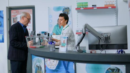 Pharmacist at drugstore counter scanning pharmaceutical items from elderly customer shopping basket. Senior man buying pain lowering medicaments in pharmacy after consulting with specialist