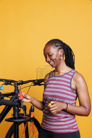 Konzentrierte afrikanisch-amerikanische Radfahrerin repariert und pflegt ein modernes Fahrrad mit einer Reihe von Werkzeugen. Lächelnde schwarze Frau arrangiert professionelle Ausrüstung zur Reparatur beschädigter Fahrräder.