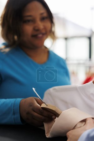 Foto de Mujer afroamericana sosteniendo múltiples camisas, comprando ropa elegante en la boutique moderna. Comprador sonriente con ganas de nuevo armario, compras de mercancía de moda y accesorios - Imagen libre de derechos