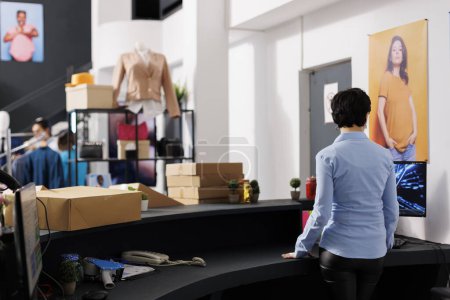 Photo for Formal worker standing at counter desk, checking online orders on computer in modern boutique. Caucasian woman preparing packages for delivery, answering customers mail in clothing store - Royalty Free Image