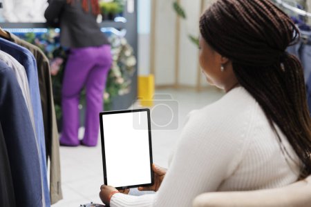 Foto de Cliente afroamericano sosteniendo tableta con pantalla táctil en blanco en el centro comercial. Mujer que utiliza el software de la aplicación en el dispositivo digital con pantalla vacía maqueta en la tienda de ropa - Imagen libre de derechos