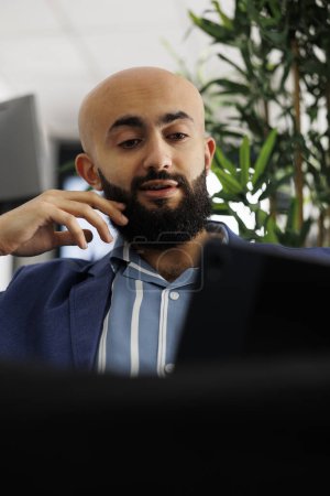 Foto de Hombre de negocios árabe que tiene videollamada con su compañero de trabajo sobre el proyecto de inicio utilizando tableta digital en el espacio de coworking. Ejecutivo discutiendo el lanzamiento del producto con el cliente en la reunión en línea - Imagen libre de derechos