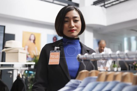 Photo for Asian woman seller working in clothing store, managing formal apparel inventory and checking shits on display rack. Shopping center employee organizing menswear garment in boutique - Royalty Free Image