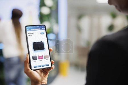 Photo for Client choosing clothes on online app, looking at modern fashion collection on mobile application. Young shopper choosing clothing items on clothes boutique website in retail shop. - Royalty Free Image