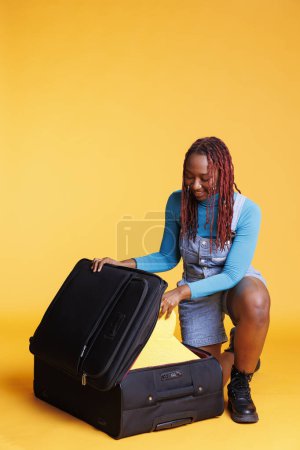 Female tourist packing bags for vacation, putting essentials and items in trolley bag before leaving on holiday trip. Young woman feeling excited about travelling, pack clothes.