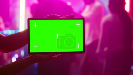 Photo for Person showing tablet with greenscreen at nightclub, being on the dance floor holding device with mockup template. Girl looking at isolated chroma key display with blank copyspace. - Royalty Free Image