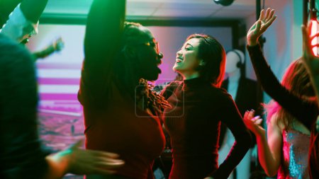 Foto de La gente moderna saltando alrededor en el club, divirtiéndose bailando en la música funky electrónica en la fiesta. Hombres y mujeres jóvenes disfrutando de la vida nocturna en la pista de baile, actuación discoteca. Trípode tiro. - Imagen libre de derechos