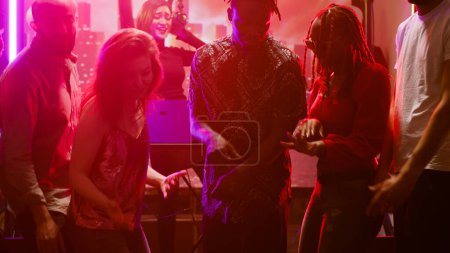 Multiethnic group of friends having fun at club, dancing together on live music in discotheque. Happy young people partying and jumping on dance floor, electronic party sounds.