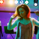 Young person dancing at nightclub, showing cool dance moves in discotheque with funky music. Cheerful girl partying and having fun at electronic party, stage lights on dance floor. Handheld shot.