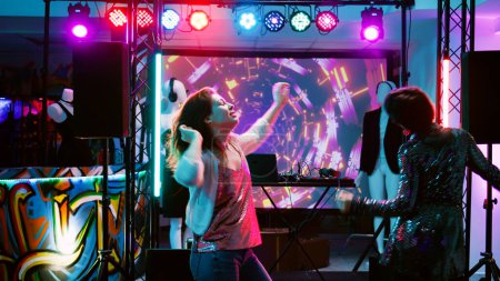 Foto de Bailarina festejando en discoteca, mostrando movimientos de baile funky en discoteca con música electrónica. Mujer joven bailando y divirtiéndose en la fiesta disco, focos en la pista de baile. Disparo de mano. - Imagen libre de derechos
