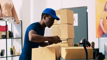 Photo for African american courier explaining distribution report to manager, checking orders details on tablet computer in modern boutique. Store employee preparing packages for delivery in shopping mall - Royalty Free Image