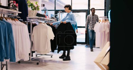 Photo for Cheerful employee arranging stylish clothes, working at modern boutique visual. Caucasian manager putting hangers with fashionable merchandise on racks in shopping centre. Fashion concept - Royalty Free Image