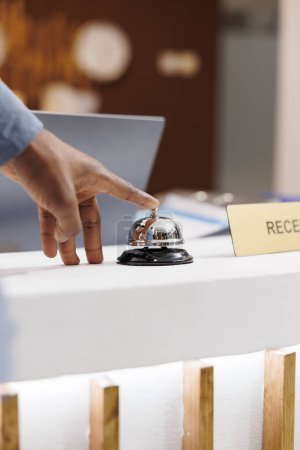 Photo for Close up of male hand pressing down front desk bell button while standing at empty reception counter, selective focus. Guest arrived at hotel, waiting for receptionist to check-in - Royalty Free Image