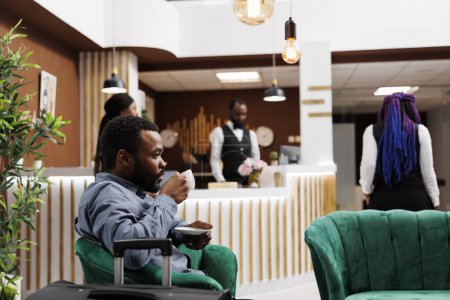 Téléchargez les photos : Homme d'affaires afro-américain buvant du café en attendant l'enregistrement dans le hall de l'hôtel. Homme noir fatigué voyageur tenant tasse d'expresso au repos après un long vol, attendant la chambre - en image libre de droit