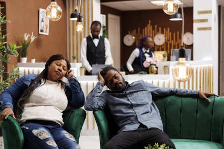 Téléchargez les photos : Le décalage horaire. Fatigué touristes afro-américains épuisés dormant dans le hall de l'hôtel après un voyage en avion longue distance, couple noir s'endormir en attendant l'enregistrement à la réception - en image libre de droit
