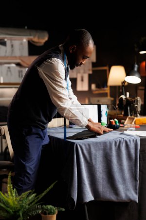 Fachkundiger Koffermacher, der im Atelierraum mit Präzision und Sachverstand am Anzug-Blazer arbeitet. Professioneller Modedesigner beendet sartorial Geschäftskleidung für Kundenauftrag