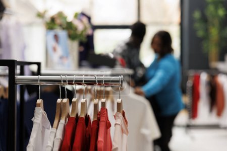 Foto de Enfoque selectivo de perchas llenas de ropa de moda en la boutique moderna, en segundo plano pareja afroamericana de compras para la camisa de moda, la comprobación de los artículos de tela. Concepto de moda - Imagen libre de derechos