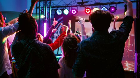 Téléchargez les photos : Des adultes joyeux s'amusent avec de la musique de DJ sur la station de panel, dansant sous des lumières disco sur la piste de danse. Jeune foule d'amis faire la fête et clubbing avec des rythmes funky modernes. Coup de main. - en image libre de droit