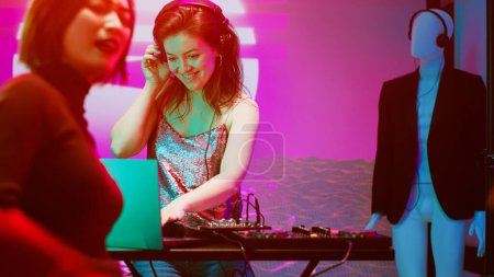 Téléchargez les photos : Fille souriante mélangeant de la musique à la station DJ, créant une atmosphère joyeuse au club sur scène. Heureuse femme moderne s'amuser avec des sons au panneau audio, clubbing avec des amis sur la piste de danse. - en image libre de droit