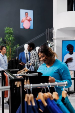 Photo for African american shopaholic woman shopping for casual wear in modern boutique, checking merchandise fabric. Stylish customer wanting to buy new fashion collection in clothing store - Royalty Free Image