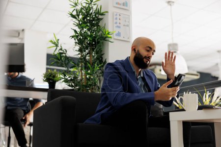 Arabe homme bavarder sur smartphone videocall et saluer salut dans le bureau d'affaires de démarrage. Équipe d'accueil des employés responsable de la vidéoconférence sur téléphone mobile dans un espace de coworking moderne