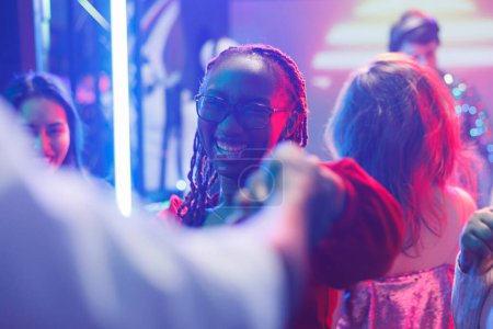 Foto de Mujer feliz bailando con amigos y festejando en la discoteca en el club nocturno. alegre sonriente joven afroamericano clubber moviéndose en pista de baile en la actuación de música electrónica - Imagen libre de derechos
