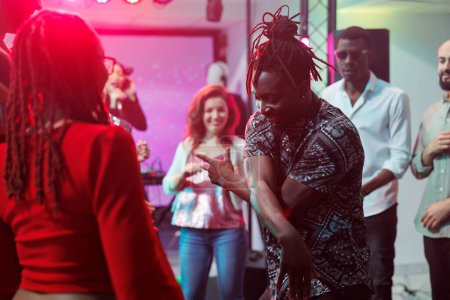 Téléchargez les photos : Couple afro-américain montrant des mouvements sur la piste de danse bondée dans une boîte de nuit. Des danseurs insouciants improvisent une bataille de danse pour les jeunes lors d'une soirée discothèque au club - en image libre de droit