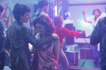 Téléchargez les photos : Des femmes dansant ensemble tout en faisant la fête et en assistant à une discothèque dans une boîte de nuit. Jeunes copines se déplaçant sur la piste de danse et et profiter du divertissement de la vie nocturne tout en clubbing - en image libre de droit