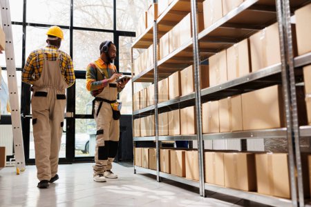 Photo for African american warehouse employee in headphones overseeing parcels security and maintenance. Post office shipment operator listening to music and working in storage room - Royalty Free Image