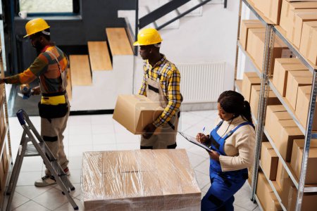Photo for Package handlers picking order and packing parcels in warehouse. All black retail storehouse employees team inspecting packages before transportation using checklist on clipboard top view - Royalty Free Image