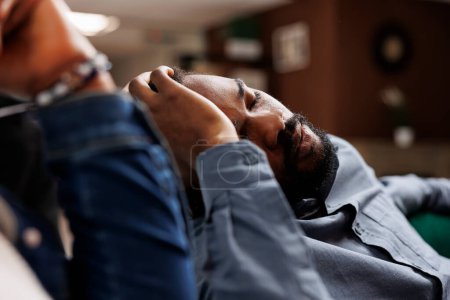 Foto de Cansado joven afroamericano agotado turista se quedó dormido después de un largo vuelo, tomando siesta en el vestíbulo del hotel. Negro chico viajero siesta mientras espera el check-in, que sufre de jet lag - Imagen libre de derechos