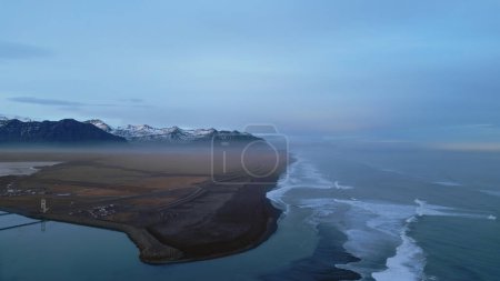 Foto de Vista aérea de la costa de hielo con famosa playa de arena negra y paisajes nórdicos, montañas nevadas y colinas. Hermosa orilla del océano con vista panorámica natural. Movimiento lento. - Imagen libre de derechos