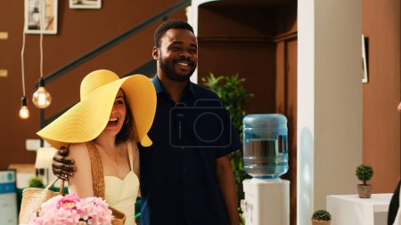 Photo for Couple arriving at exotic resort for summertime vacation, talking to receptionist about room reservation. People on honeymoon holiday preparing for check in service at seaside hotel. - Royalty Free Image