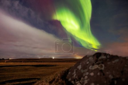 Foto de Las tierras altas islandesas con luces boreales son visibles. Increíble paisaje creado por aurora boreal bajo el cielo lleno de estrellas. Impresionante evento natural con colores vibrantes y rocas cubiertas de nieve. - Imagen libre de derechos